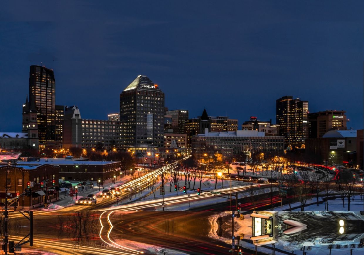 Evening view of downtown St. Paul, Minnesota, with snow-covered streets and glowing trails of car lights weaving through the city as the Travelers building and other high-rises illuminate the skyline — highlighting the vibrant urban community served by Darryl Spence Ministries of St. Paul, Minnesota. Visit darrylspenceministries.com to learn more!